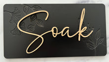 Load image into Gallery viewer, Transform your bathroom into a serene oasis with these Beautiful Relax, Soak, Unwind signs. Crafted from high-quality wood, each sign features delicate embossing of subtle flowers and foliage, creating a soft, nature-inspired background. Perfectly sized at 11 1/2” long x 6” tall, these signs effortlessly add a calming spa-like touch to any space. Whether you're creating a tranquil retreat or enhancing your bathroom's décor, these elegant signs bring a sense of peace and relaxation to your home.