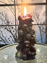 Load image into Gallery viewer, Unleash the spooky vibe with our one-of-a-kind bleeding skull beeswax candle. As it burns, watch in awe as the 'blood' oozes and the skulls roll off onto the plate, adding an eerie touch to your Halloween decorations. The glowing eyes and piles of skulls and bones make this pillar candle a must-have for gothic and fall decor. Perfect for gifting to skull-loving friends or for adding a touch of horror to any room. Get yours now and bring the creepy factor to your home!