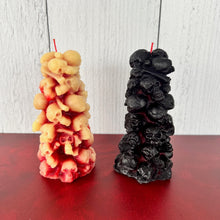 Load image into Gallery viewer, Unleash the spooky vibe with our one-of-a-kind bleeding skull beeswax candle. As it burns, watch in awe as the 'blood' oozes and the skulls roll off onto the plate, adding an eerie touch to your Halloween decorations. The glowing eyes and piles of skulls and bones make this pillar candle a must-have for gothic and fall decor. Perfect for gifting to skull-loving friends or for adding a touch of horror to any room. Get yours now and bring the creepy factor to your home!