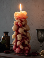 Load image into Gallery viewer, Unleash the spooky vibe with our one-of-a-kind bleeding skull beeswax candle. As it burns, watch in awe as the 'blood' oozes and the skulls roll off onto the plate, adding an eerie touch to your Halloween decorations. The glowing eyes and piles of skulls and bones make this pillar candle a must-have for gothic and fall decor. Perfect for gifting to skull-loving friends or for adding a touch of horror to any room. Get yours now and bring the creepy factor to your home!
