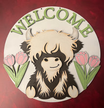 Load image into Gallery viewer, Welcome guests in the sweetest way with this adorable Highland Cow Door Hanger! Featuring a charming Highland cow design with WELCOME displayed across the top and cheerful tulips on each side, this piece is the perfect accent to brighten your entryway and celebrate the beauty of spring.
