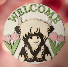 Load image into Gallery viewer, Welcome guests in the sweetest way with this adorable Highland Cow Door Hanger! Featuring a charming Highland cow design with WELCOME displayed across the top and cheerful tulips on each side, this piece is the perfect accent to brighten your entryway and celebrate the beauty of spring.