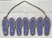 Load image into Gallery viewer, Add a bit of summer to your entry way with this Flip Flop Welcome Door Hanger Sign.  These adorable flip flops spelling out WELCOME invite guest into your home.  Perfect for lake houses, beach retreats or just to add a bit of summer decor.  Also available in Beach Bum design.  A line of seven flip flops with the words Welcome or Beach Bum across the bottom.