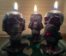 Load image into Gallery viewer, Each beeswax candle measures 4" tall x 2 3/16" wide, and weighs approximately 2 ounces, makin them the perfect size for any room in your home. The three skulls feature a unique design, embodying the classic "see no evil, hear no evil, speak no evil" phrase. Available in a black exterior with red core or a yellow exterior with red core.  Image shows all three candles burning.