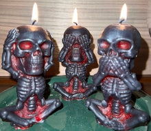 Load image into Gallery viewer, Each beeswax candle measures 4" tall x 2 3/16" wide, and weighs approximately 2 ounces, makin them the perfect size for any room in your home. The three skulls feature a unique design, embodying the classic "see no evil, hear no evil, speak no evil" phrase. Available in a black exterior with red core or a yellow exterior with red core.  Picture of all three candles burning.
