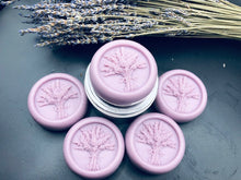 Load image into Gallery viewer, Purple round bar of lotion with lavender bouquet design in the middle. 3.5 oz approx. weight. These handy lotion bars are great when you're on the go or for everyday use! Natural body heat slightly melts a bit of the lotion onto your hands. Great for elbows and dry areas. It leaves your skin feeling smooth and hydrated. The beeswax adds a barrier of protection that keeps the lotion where you put it longer. Made by hand in the USA.