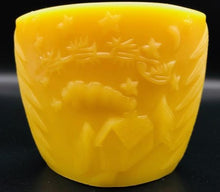 Load image into Gallery viewer, Oval all natural beeswax candle with Santa and his reindeer flying over a house in the woods. Pine tree design adorns the edges of the candle. Handmade in the USA.