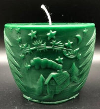 Load image into Gallery viewer, Oval all natural beeswax candle with Santa and his reindeer flying over a house in the woods. Pine tree design adorns the edges of the candle. Handmade in the USA. Green