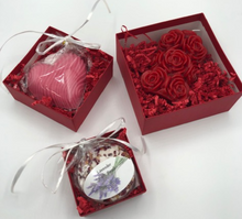 Load image into Gallery viewer, That special someone is sure to feel the love this Valentines Day when they open this fantastic Valentines Day Gift Box Trio.  A stack of 3 red boxes tied with a white ribbon.  Set contains 1 Red Beeswax Rose Pillar Candle, 1 Lavender Bath Bomb & 1 Heart Shaped Goat's Milk Soap in either Lavender or Rose Geranium scents.