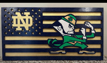 Load image into Gallery viewer, A wooden cutout wall sign featuring a stylized American flag with navy blue and natural wood stripes, a navy canton with a gold 'ND' , and a green  leprechaun character flexing his arm.
