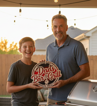 Load image into Gallery viewer, Give Dad's favorite grilling space a little personality with our Dad's Bar &amp; Grill – Good Eats, Smoked Meats Sign! Whether he's the family grill master, king of the smoker, or simply loves spending weekends cooking up something delicious, this handmade sign is a fun way to celebrate his love of BBQ.
