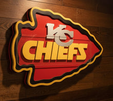 Load image into Gallery viewer, A  Chiefs shield-shaped wall sign featuring the team name in yellow and a white KC  on a red and orange background, with a black and gold outline
