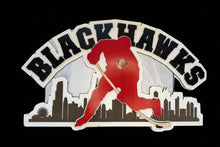 Load image into Gallery viewer, A decorative Chicago Blackhawks wooden sign featuring a red hockey player silhouette, black 'BLACKHAWKS' lettering, and a black city skyline on a white backing, shown against a blue gradient background.
