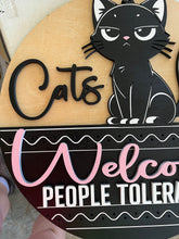 Load image into Gallery viewer, Let guests know exactly where they stand with this hilarious “Cats Welcome, People Tolerated” door hanger sign! Featuring an adorable black cat giving the ultimate snide side-eye look, this fun and sassy sign is the perfect addition to any cat lover’s home décor.

