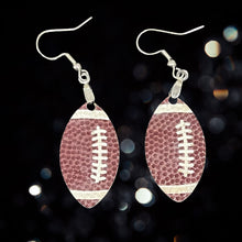 Load image into Gallery viewer, Score big on game day with our stylish Football Earrings! Designed with a realistic football-textured finish, these earrings are the perfect way to showcase your love for the game and your team spirit. Lightweight and easy to wear, they feature a sleek 1.5&quot; football-shaped design that adds the perfect sporty touch to any outfit. 
