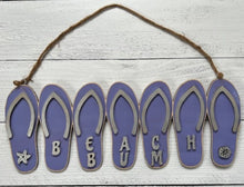 Load image into Gallery viewer, Add a bit of summer to your entry way with this Flip Flop Welcome Door Hanger Sign.  These adorable flip flops spelling out WELCOME invite guest into your home.  Perfect for lake houses, beach retreats or just to add a bit of summer decor.  Also available in Beach Bum design.  A line of seven flip flops with the words Welcome or Beach Bum across the bottom.
