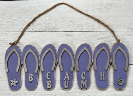 Add a bit of summer to your entry way with this Flip Flop Welcome Door Hanger Sign.  These adorable flip flops spelling out WELCOME invite guest into your home.  Perfect for lake houses, beach retreats or just to add a bit of summer decor.  Also available in Beach Bum design.  A line of seven flip flops with the words Welcome or Beach Bum across the bottom.