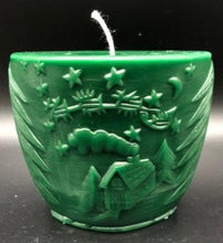 Load image into Gallery viewer, Oval all natural beeswax candle with Santa and his reindeer flying over a house in the woods. Pine tree design adorns the edges of the candle. Handmade in the USA. Green
